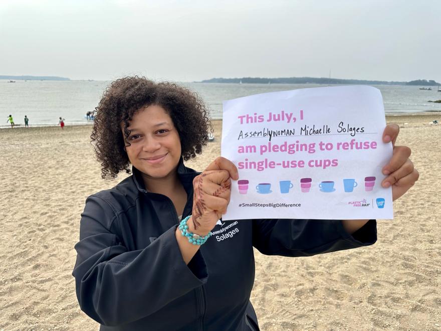 Person holding up a Plastic Free July pledge on a beach