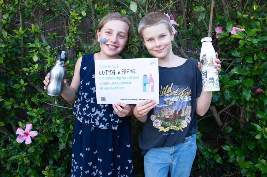 Children holding up a Plastic Free July pledge and holding water bottles