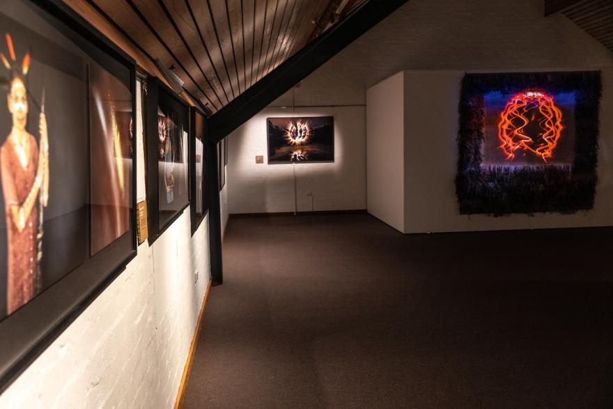 Gallery hallway with framed photographs on one wall and glowing artworks on another.