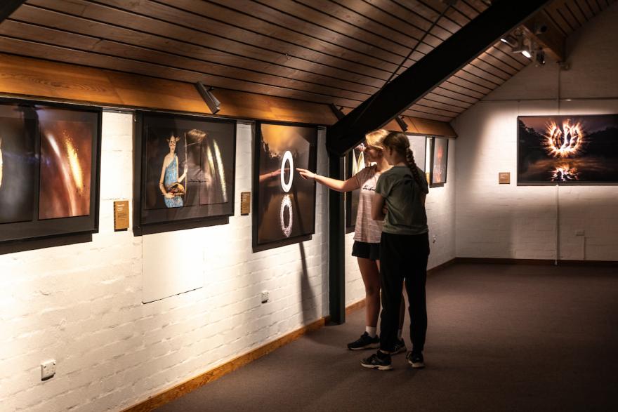 Two people in a gallery examining framed photographs on a wall.