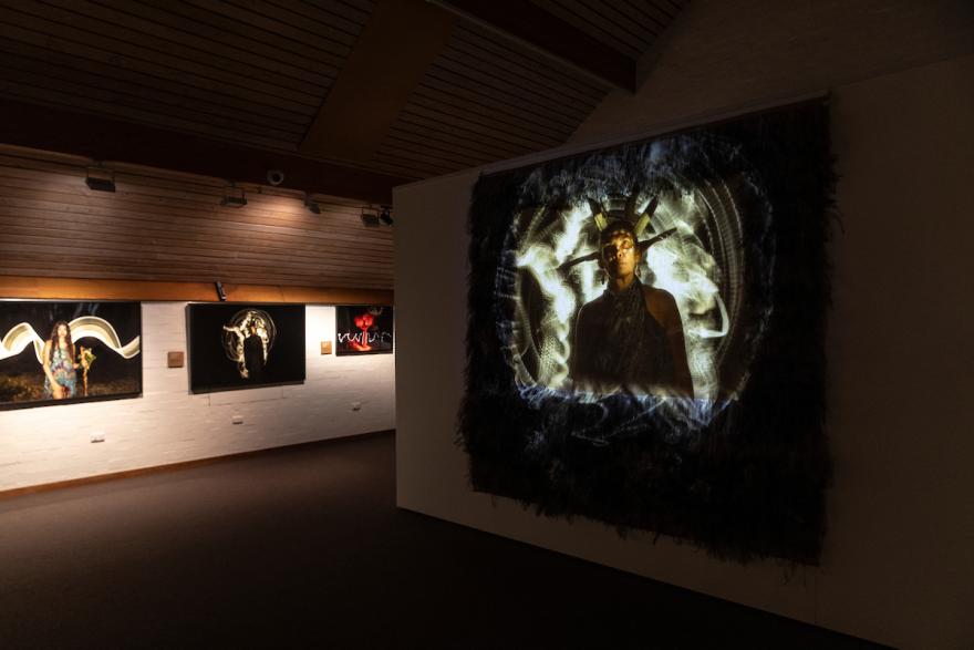 A gallery with framed photographs on a white wall and a projection of a person onto a textured backdrop.