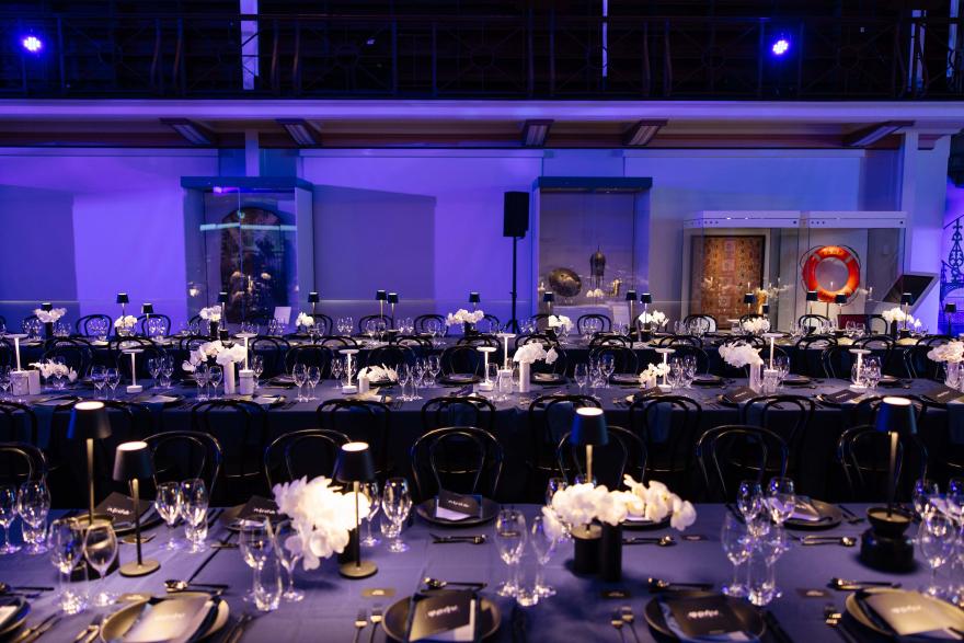 Elegantly set dining tables with lamps and white flowers, surrounded by museum exhibits.
