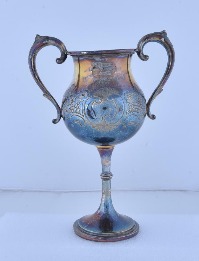 A shot of the trophy engraved with 'Won by M. Perry. Best Player Football Match Economic v Foys.'