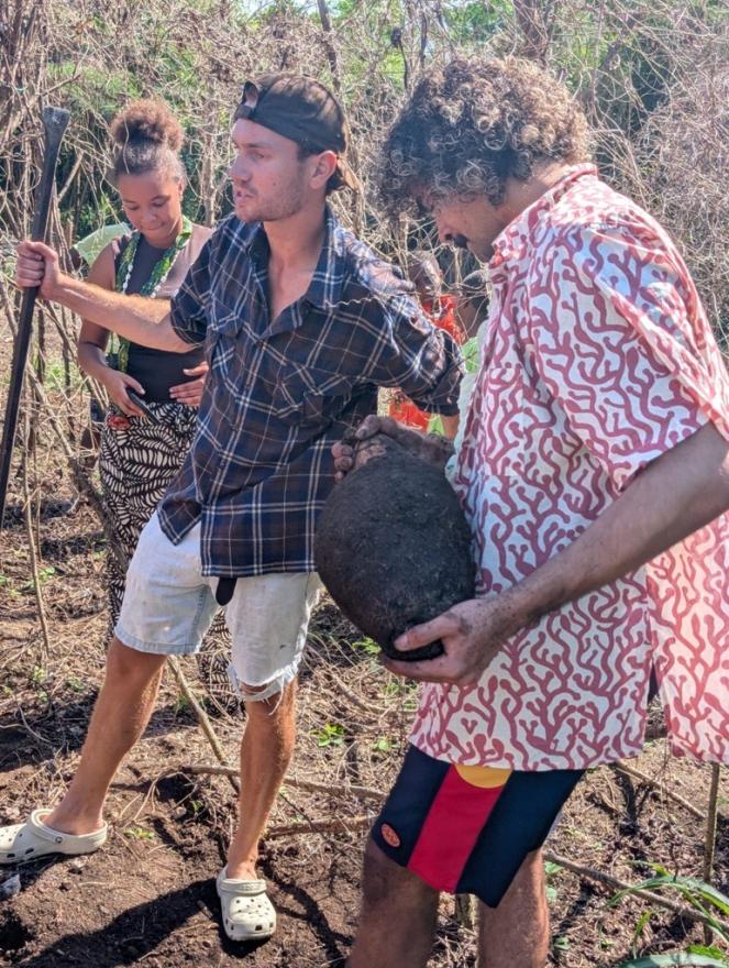 Three young people standing amongst bushland, one holds a giant rock.