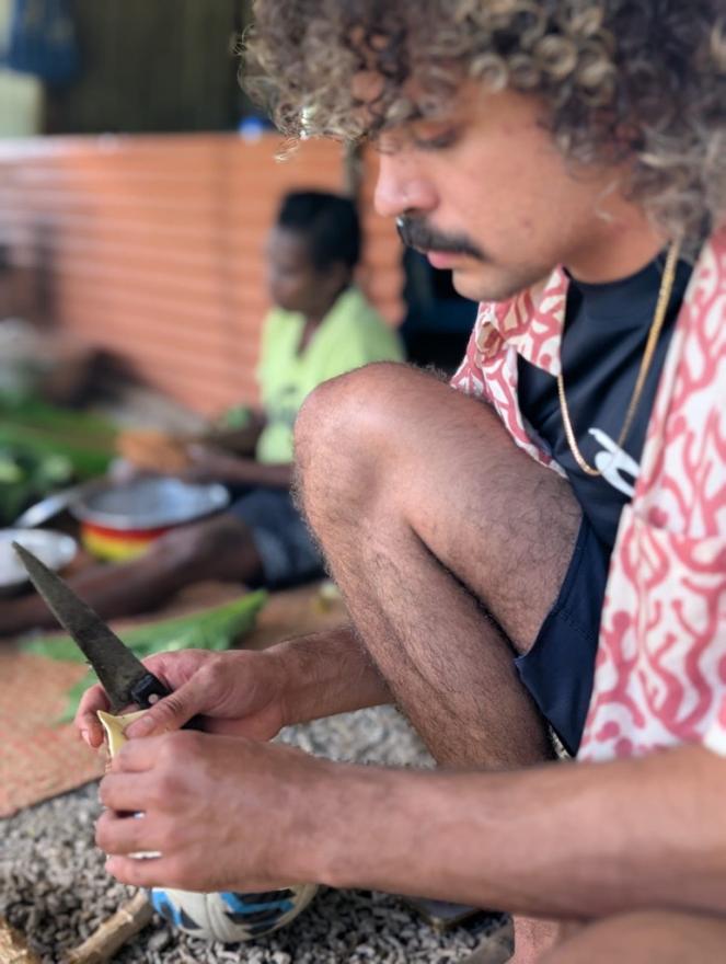 A young man kneeling down, holding a knife as he creates something unseen.