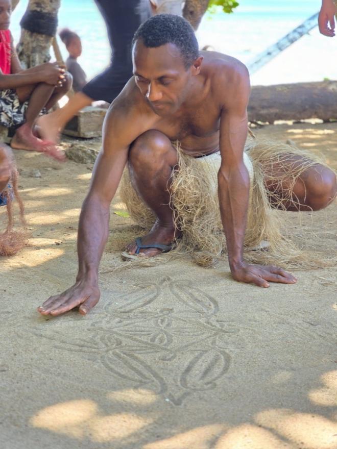 An Indigenous man drawing in the sand.