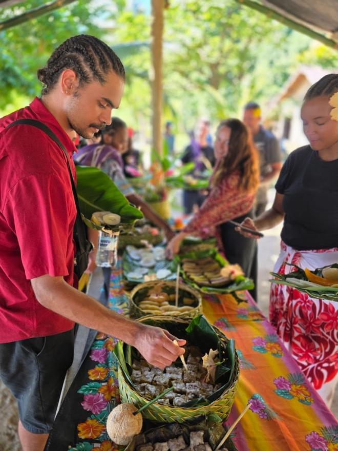 A young Indigenous man tasting food from a bowl on a table filled with traditional meals.