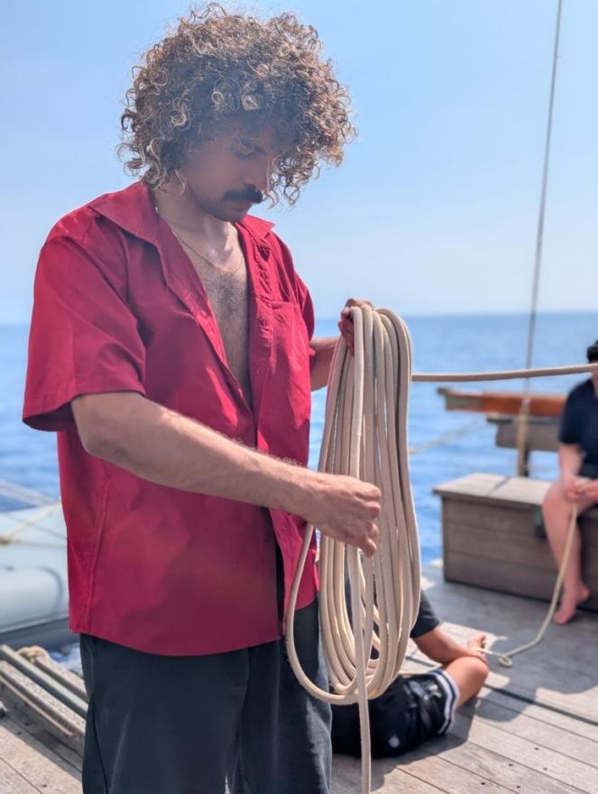A young Indigenous man coiling rope on a boat.