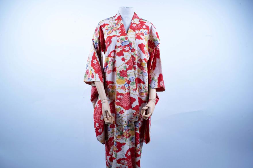 A red and white kimono, adorned with a yellow, blue, and green floral pattern, is displayed on a mannequin.