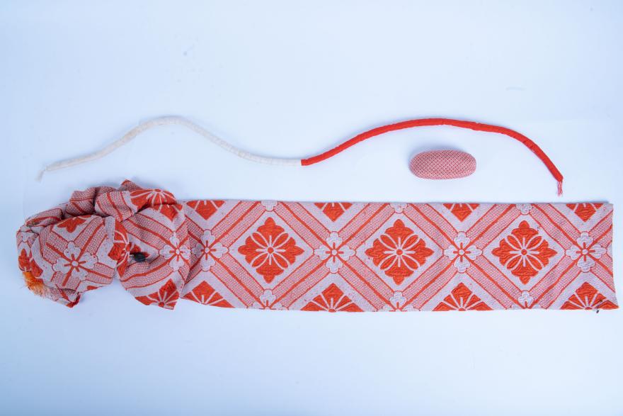 An orange and white patterned Obi, Obi Makura, and Marugake Obijime, displayed flat.