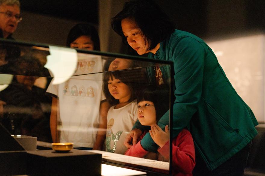 A mother and daughter gaze at objects through the glass of a Museum exhibition.