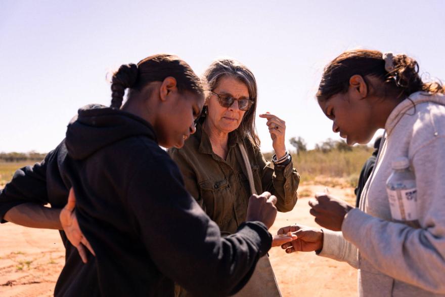 Three people standing closely together outdoors on a sunny day, examining small objects in their hands.
