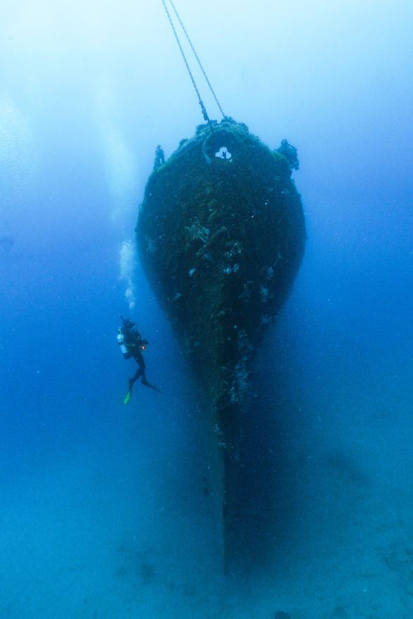 Underwater photo of a man diving next to a submerged ship