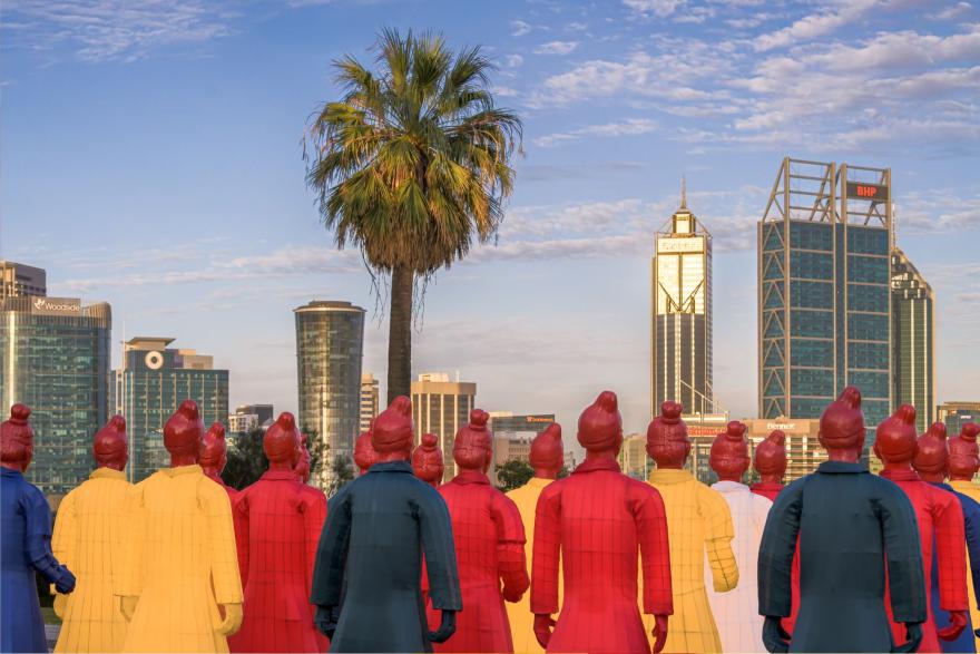 Colourful lanterns resembling Terracotta Warriors in red, yellow, and blue facing the Perth city skyline with tall buildings and a palm tree.