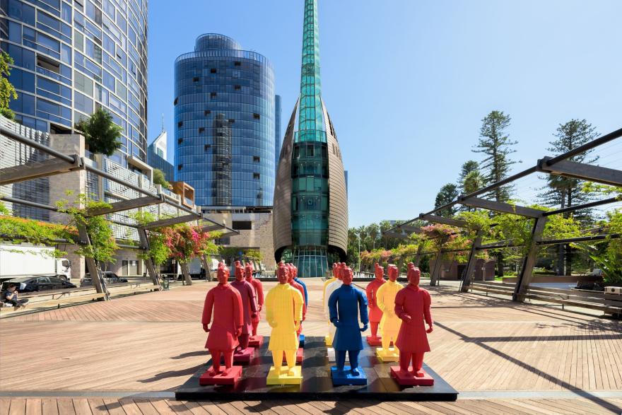 Colourful lanterns resembling Terracotta Warriors arranged on a wooden deck, with modern buildings and the Bell Tower in the background.