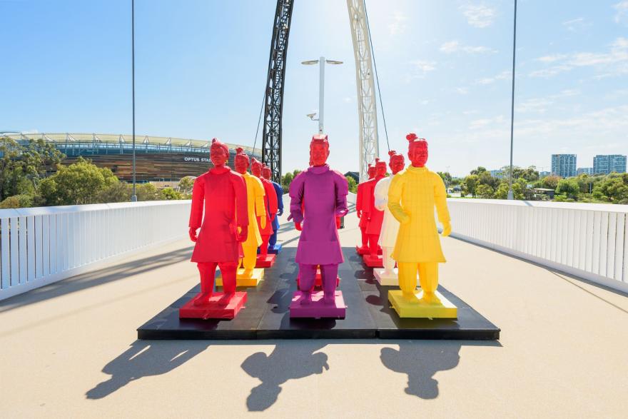 Colourful lanterns resembling Terracotta Warriors in red, yellow, and purple displayed on a bridge, with Optus Stadium visible in the background.