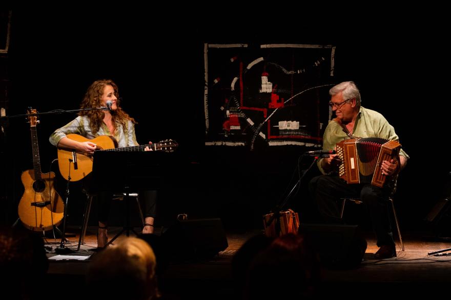 Two musicians performing onstage, one playing guitar and the other playing an accordion.