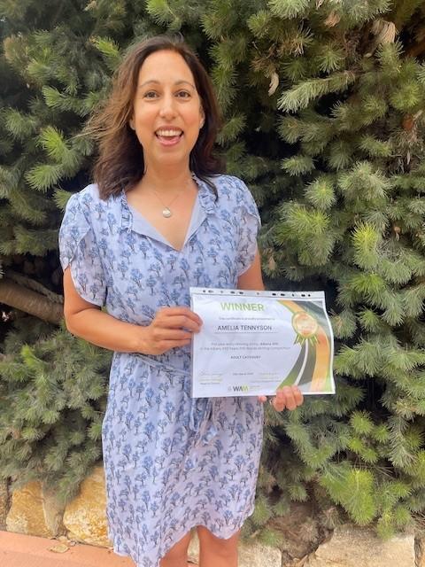 A woman holding a certificate that reads winner in front of a bush