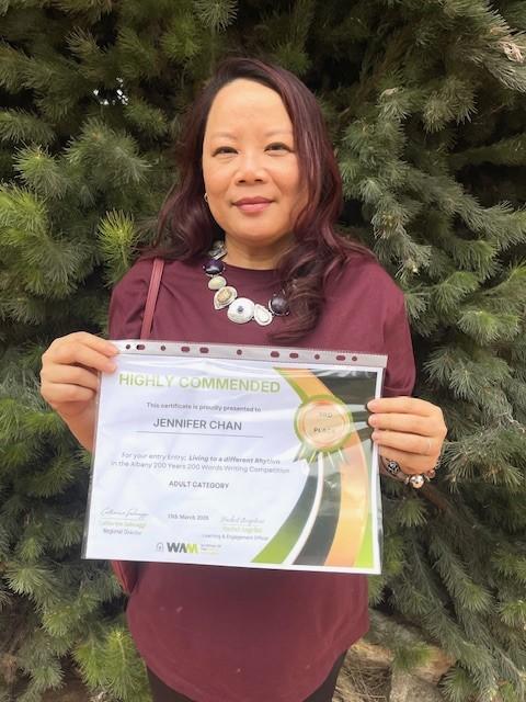 A woman holding a certificate that reads highly commended in front of a bush