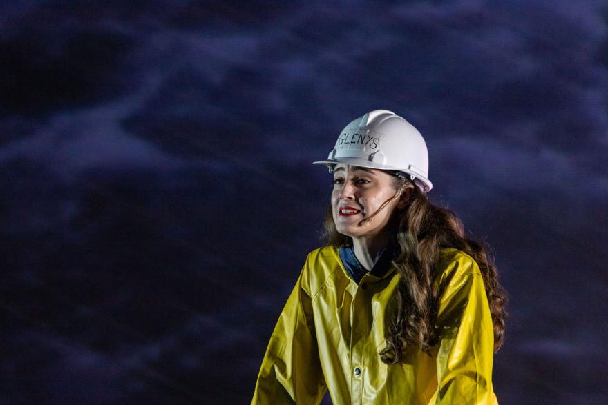 a person with long brown hair wears a white hardhat and a yellow rain jacket