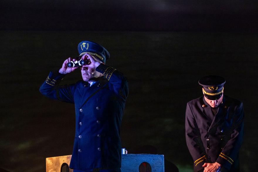 two people dressed in sailors uniform. one is looking out in the distance using binoculars and the other has their head lowered looking down