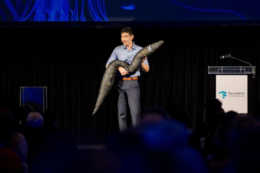 A man on stage holding a long worm prop