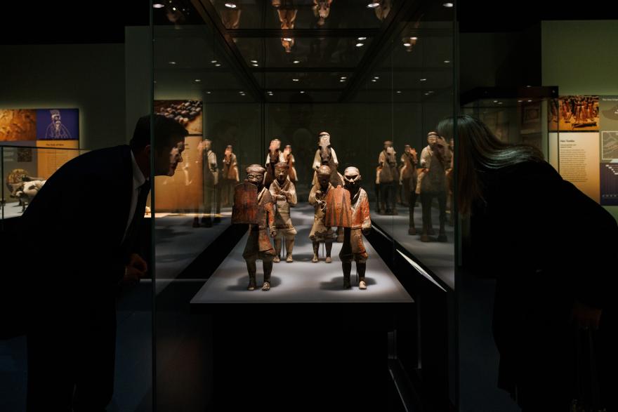Two people looking into either side of a glass case holding ancient Chinese statues