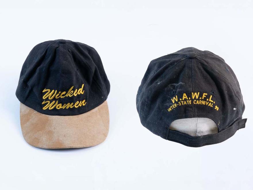 The front and back of a black baseball cap with beige brim. On the front is a gold logo for "Wicked Women", on the back is gold text reading "W.A.W.F.L Inter-state carnival 99"