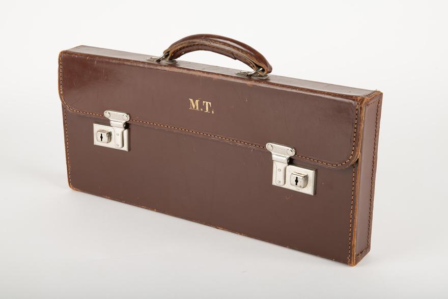 A brown leather suitcase with two clasps and gold initialism reading MT