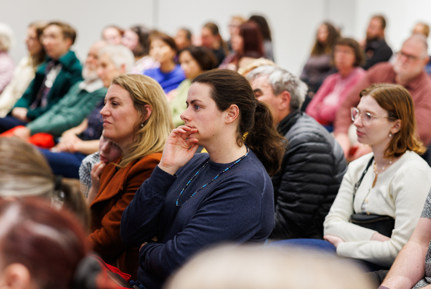 Audience members seated at a talk or presentation, listening attentively in a conference room.