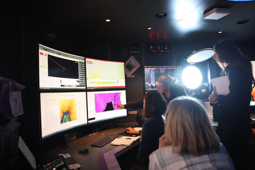 A group of scientists looking at screens inside the OeanXplorer vessel