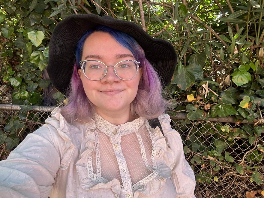 A woman with purple hair, wearing a hat