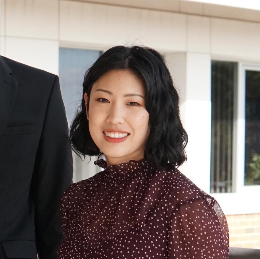 A woman with short black hair, wearing a burgundy dress