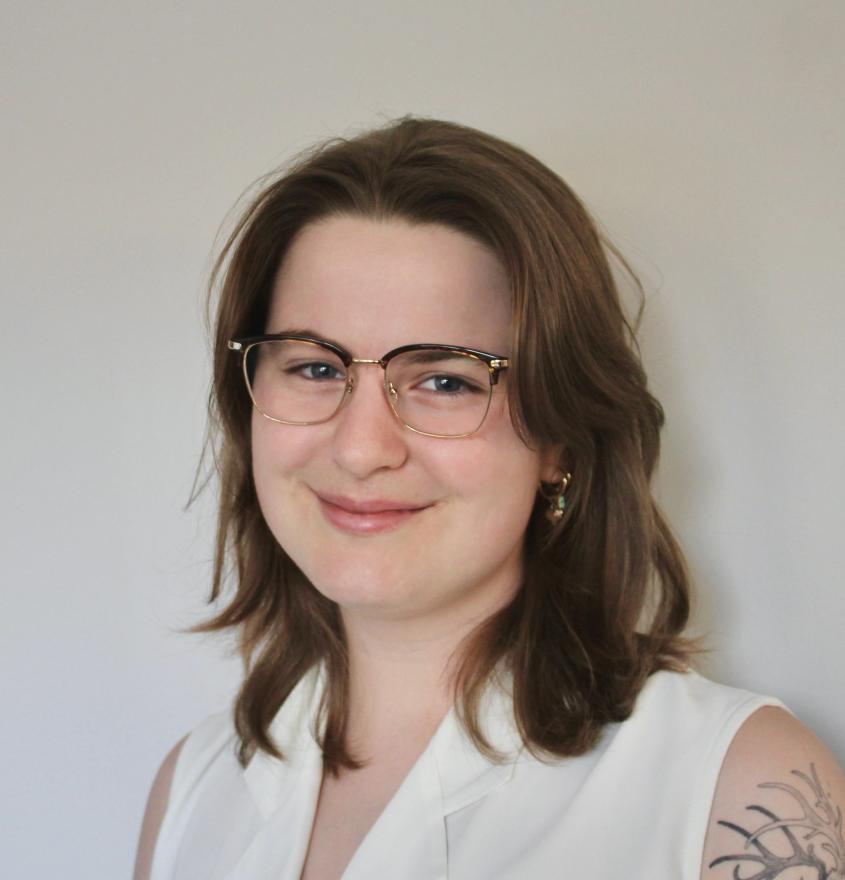 A woman wearing glasses and a white shirt, with shoulder length brown hair
