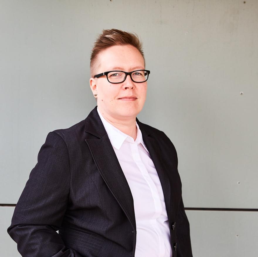 A person with very short hair, wearing glasses and a blazer