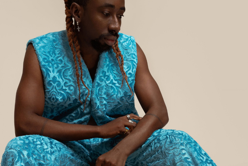 Male model in blue vest and pants posing sitting down.