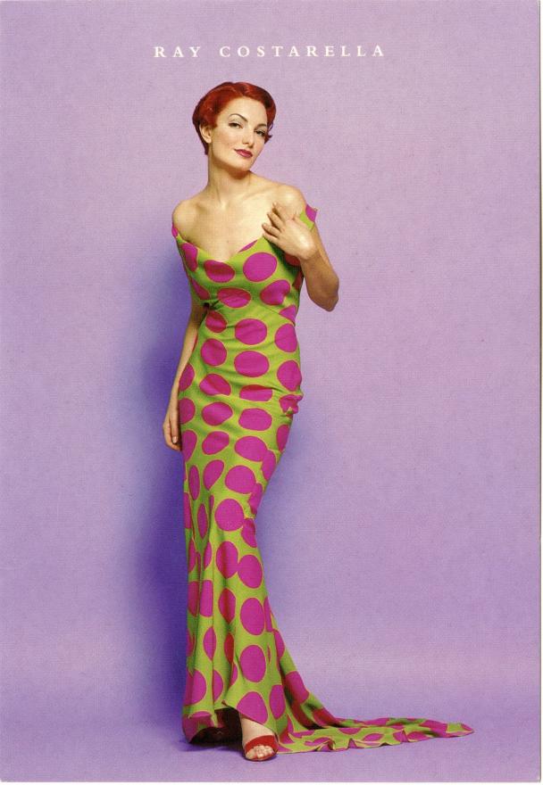 Model with red hair poses for photo in a long sleeveless green dress with pink polka dots