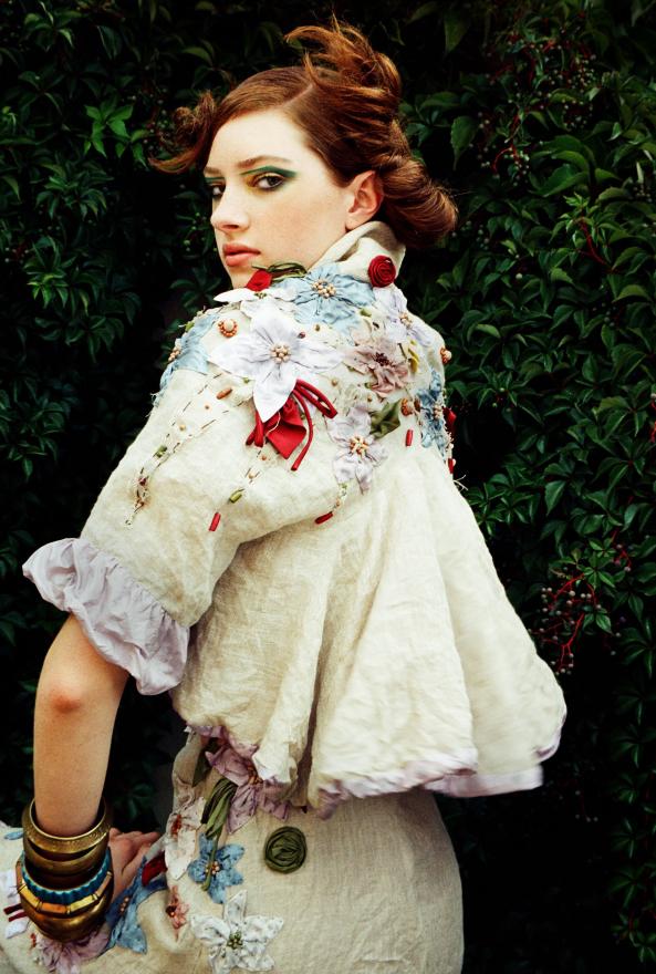 Model with red hair poses for photo in a cream outfit with ruffles and embellished with flowers