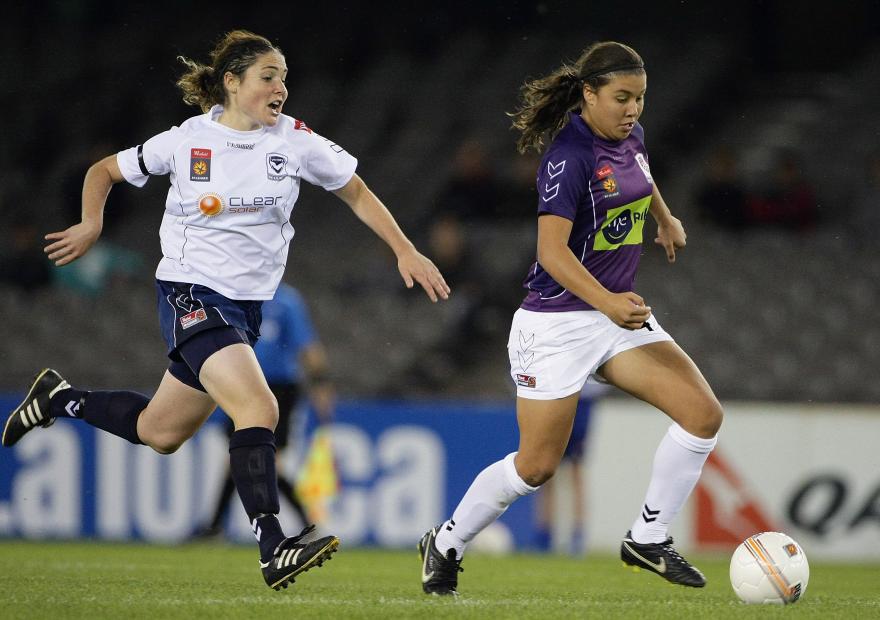 Perth Glory player dribbling the ball during a women's football match while pursued by an opposing player.
