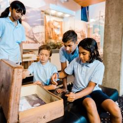 Seated children in school uniform look inside an old-fashioned suitcase