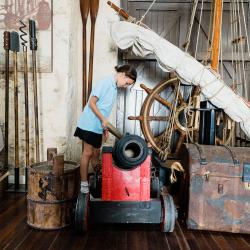 A small girl wearing blue peers over a black and red cannon.