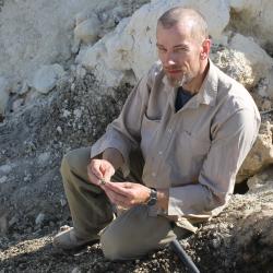 A man in light brown expedition clothing sits on rocks outdoors