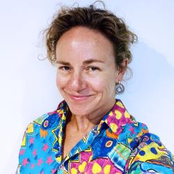 A person smiling, wearing a very colourful, heavily patterned shirt