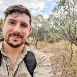 A person with dark hair stands in the bush, wearing a khaki shirt.