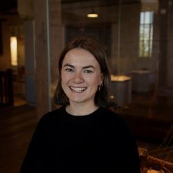 A portrait of a person wearing a black jumper in a dark Museum space