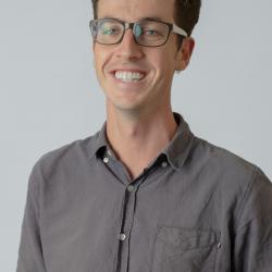 A picture of a person with short brown hair wearing glasses and a grey button up shirt