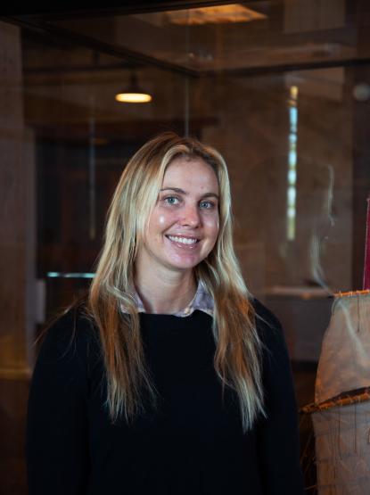 A person with long blonde hair smiles at the camera, wearing a dark jumper and collared shirt