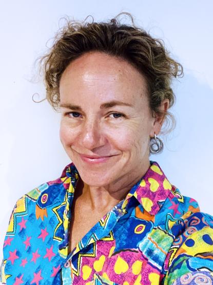 A person smiling, wearing a very colourful, heavily patterned shirt