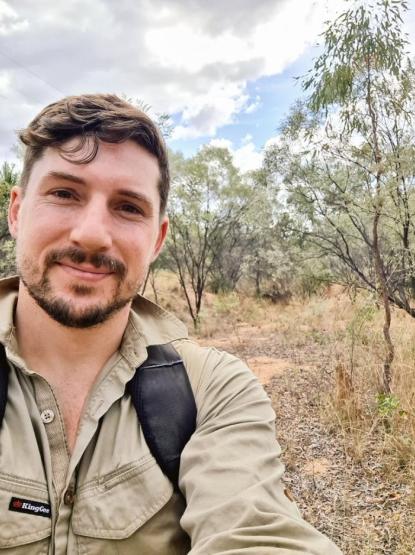 A person with dark hair stands in the bush, wearing a khaki shirt.