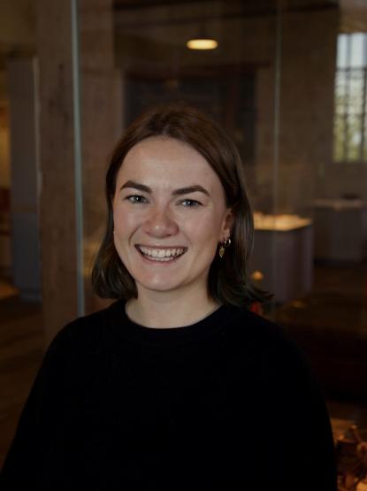 A portrait of a person wearing a black jumper in a dark Museum space